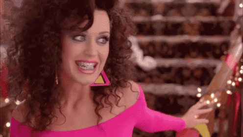 a woman with curly hair is wearing a pink off the shoulder top .