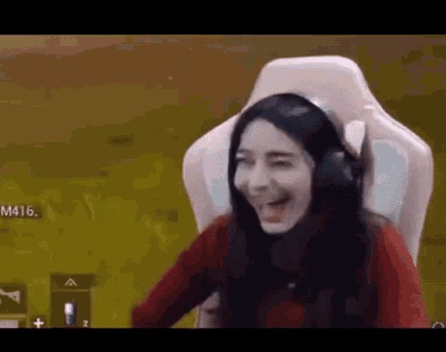 a woman wearing headphones is sitting in a pink gaming chair and laughing .