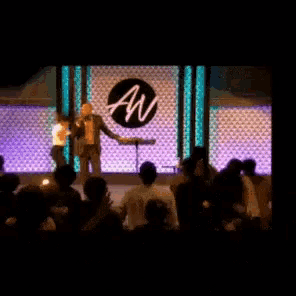 a man is giving a speech in front of a crowd with an aw logo in the background