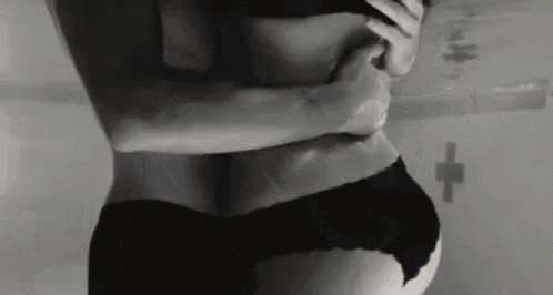 a black and white photo of a woman in black underwear hugging a man in a bathroom .