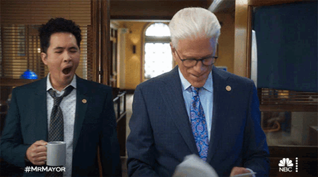 a man in a suit yawning next to another man in a suit and tie