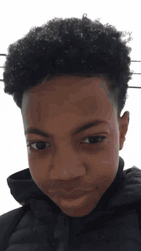 a young boy with curly hair is wearing a black jacket and making a funny face