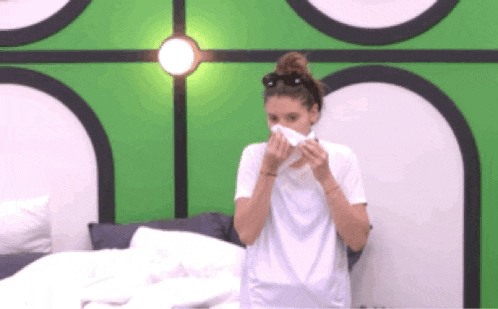 a woman in a white shirt is blowing her nose in front of a green wall