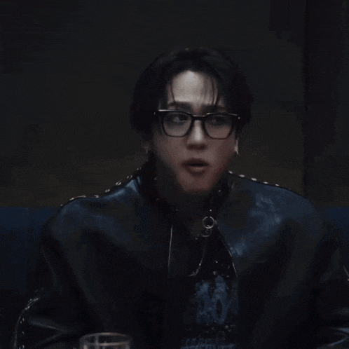 a man wearing glasses and a black leather jacket looks at the camera