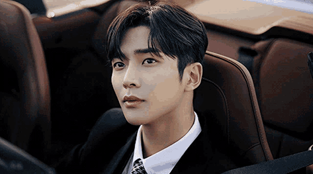 a young man in a suit and tie is sitting in a car