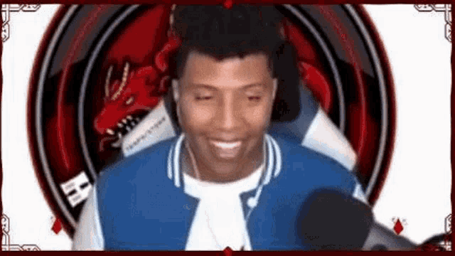 a man in a blue jacket is smiling while sitting in front of a microphone in front of a dragon .