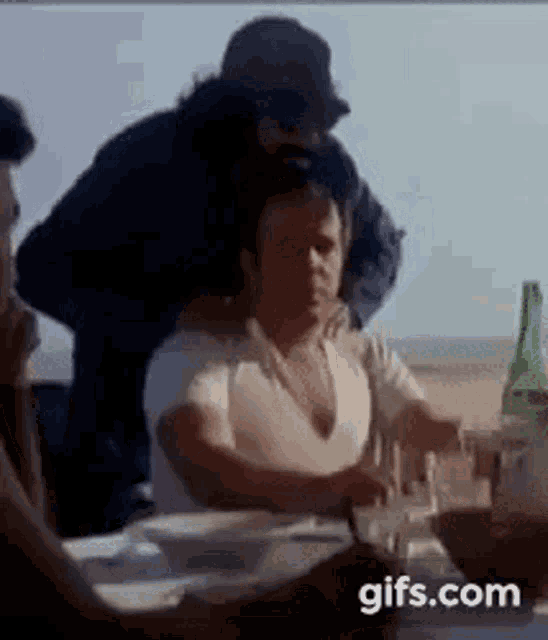 a group of people are sitting at a table with a bottle of beer .