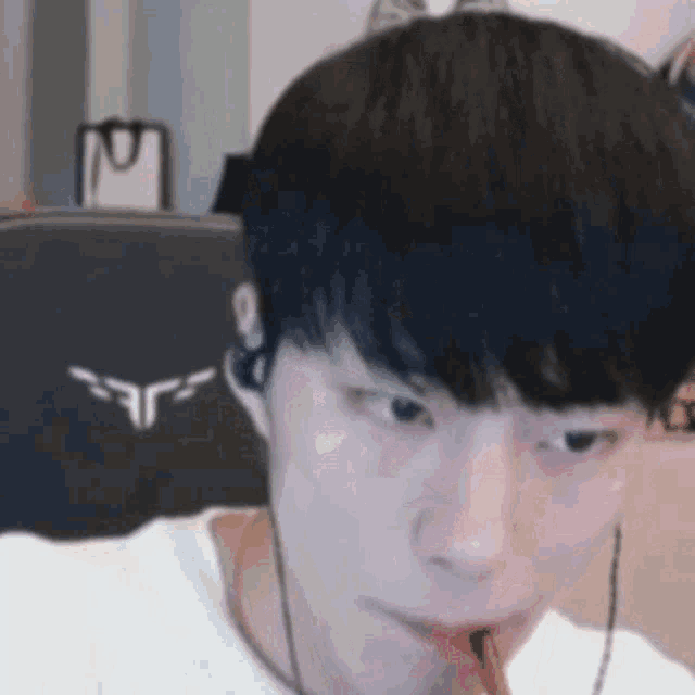 a man wearing headphones and a white shirt is eating a candy bar while sitting in a chair .