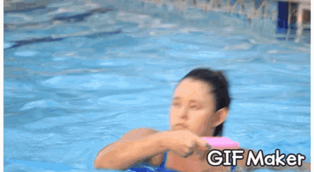 a woman in a blue bathing suit is swimming in a pool with a gif maker watermark above her