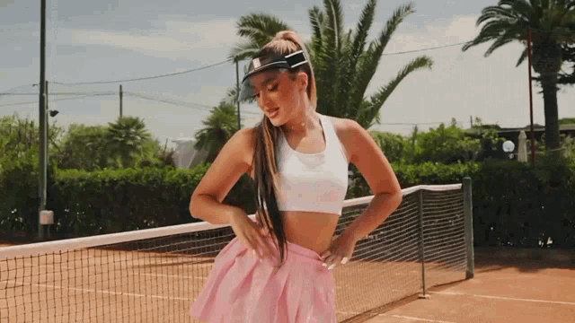 a woman wearing a white top and pink skirt is standing on a tennis court