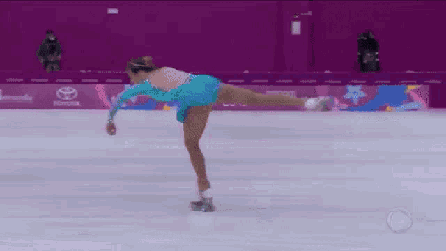 a woman in a blue dress is ice skating on a rink with a toyota sign in the background .