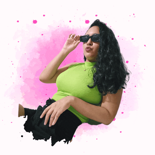 a woman wearing sunglasses and a green top is laying down on a pink background