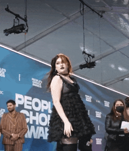 a woman in a black dress stands in front of a people 's choice awards sign