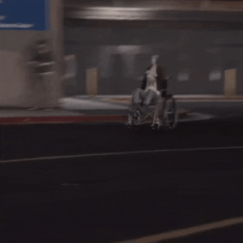 a man in a wheelchair is driving down a dark street .