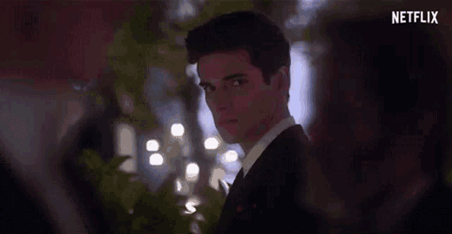 a man in a suit and tie is standing in front of a tree and looking at the camera .
