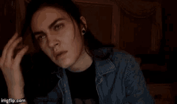 a woman with long hair and piercings is looking at the camera while wearing a denim jacket and a black shirt .
