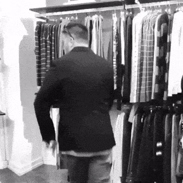 a man in a black jacket is standing in front of a rack of clothing