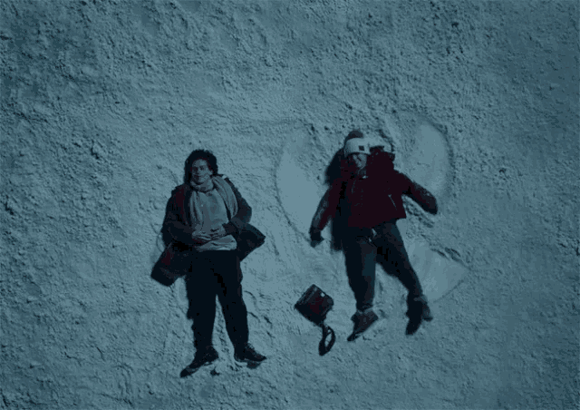 two people laying in the snow making a heart shape
