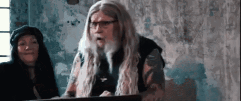 a man with long hair and glasses is standing in front of a podium .