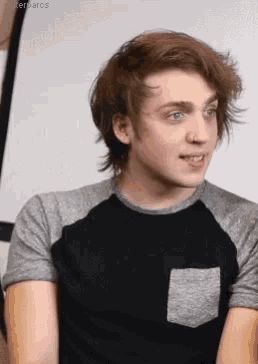 a young man with long hair and blue eyes is wearing a black and gray t-shirt .