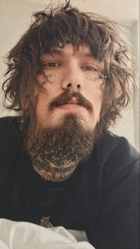 a man with curly hair and a beard has a tattoo on his forehead