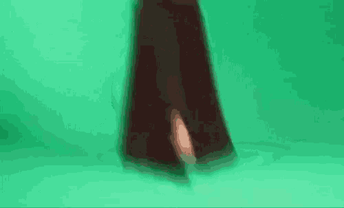 a woman in a long black skirt is walking on a green screen .