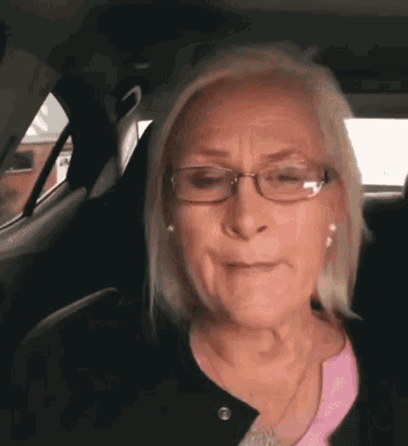 a woman is sitting in the back seat of a car wearing glasses and a pink shirt .
