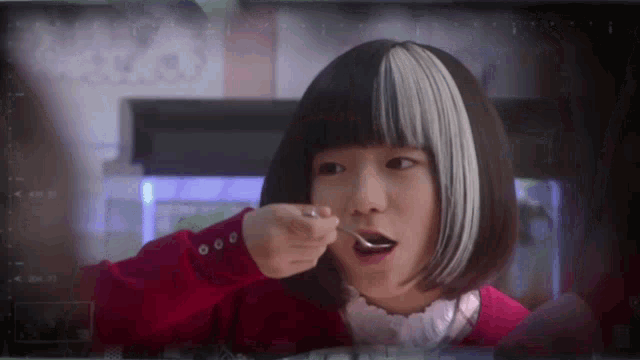 a girl with black and white hair is holding a spoon to her mouth