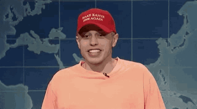 a man wearing a red hat and an orange shirt is smiling in front of a map of the world .