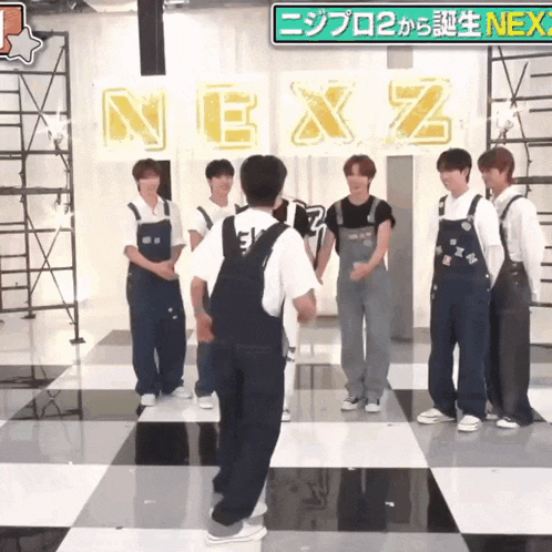 a group of young men standing on a checkered floor in front of a sign that says nexz