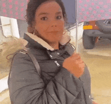 a woman in a black jacket is holding an umbrella in front of a car .