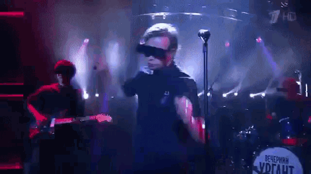 a man wearing sunglasses is singing into a microphone in front of a drum set that says " вечерняя " on it