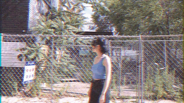 a woman in a blue tank top stands in front of a chain link fence with a sign that says " no parking "