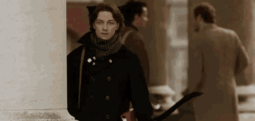 a woman in a black coat and scarf is walking down a sidewalk .