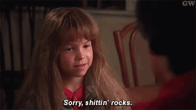 a little girl is sitting at a table talking to a man and saying sorry , shittin ' rocks .