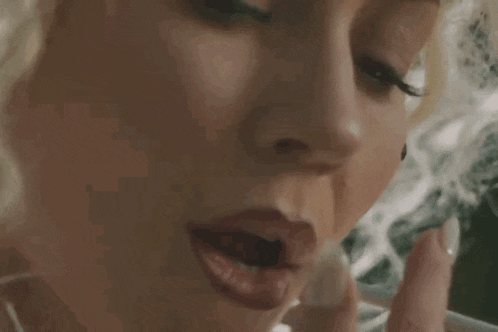 a woman is smoking a cigarette in a close up of her face .