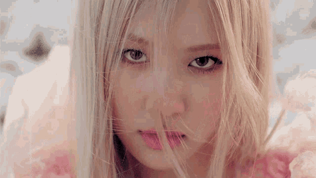 a close up of a woman 's face with long blonde hair and a pink dress .