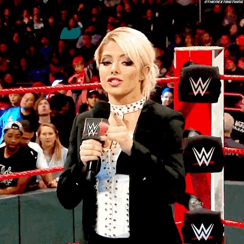 a woman is standing in a wrestling ring holding a microphone and giving a thumbs up