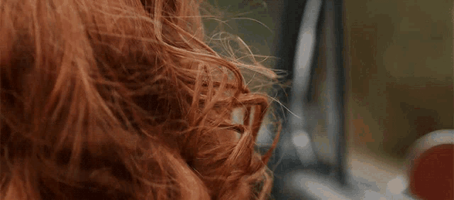 a woman 's hair is blowing in the wind while looking out of a car window .