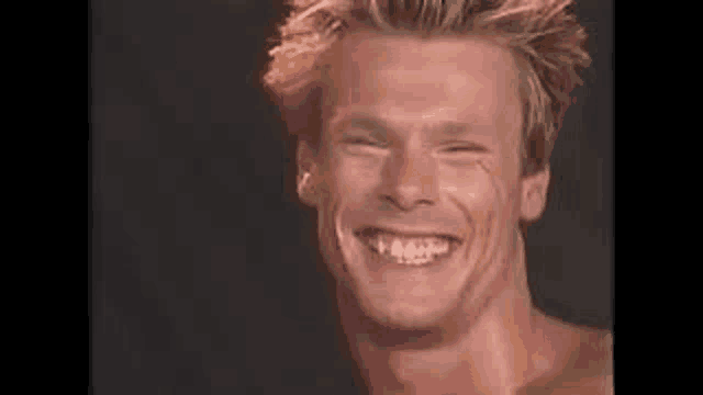 a man without a shirt is smiling and making a funny face .