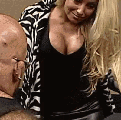 a woman with a large breast is standing next to a bald man wearing glasses