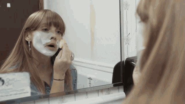 a woman is applying a shaving cream to her face in front of a bathroom mirror