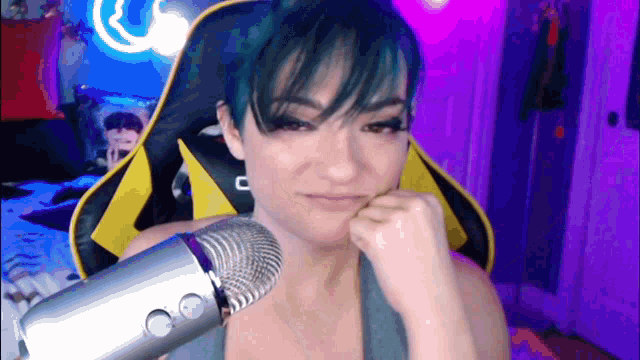 a woman with short blue hair is sitting in front of a microphone