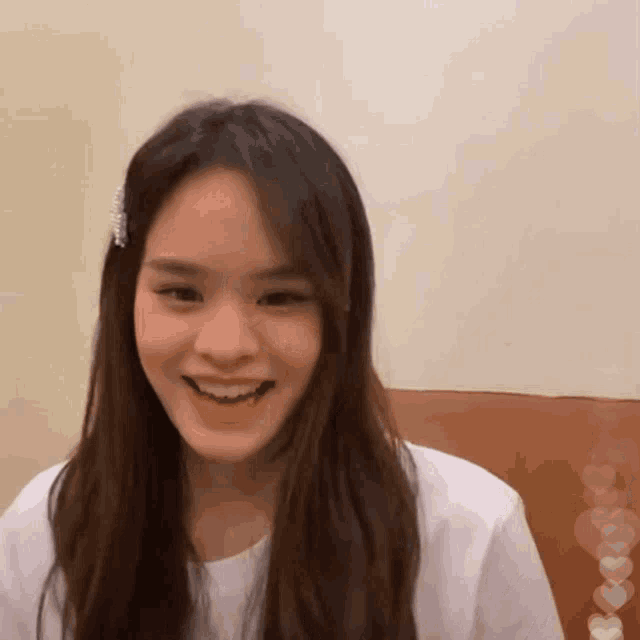 a girl with long brown hair wearing a white shirt smiles
