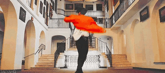 a man in an orange sweater is dancing in a large room