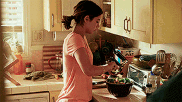 a woman in a pink shirt is preparing food in a messy kitchen
