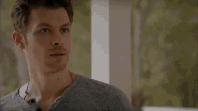 a man in a grey shirt is standing on a porch looking at something .