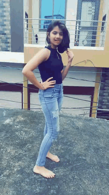 a woman in a black top and blue jeans stands on a concrete surface