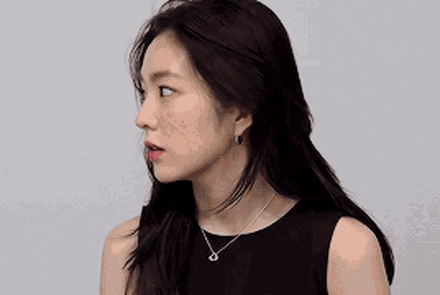 a woman wearing a black dress and a necklace with a heart on it is looking at the camera .