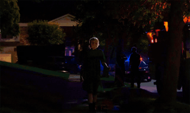 a woman in a black shirt is walking down a dark street